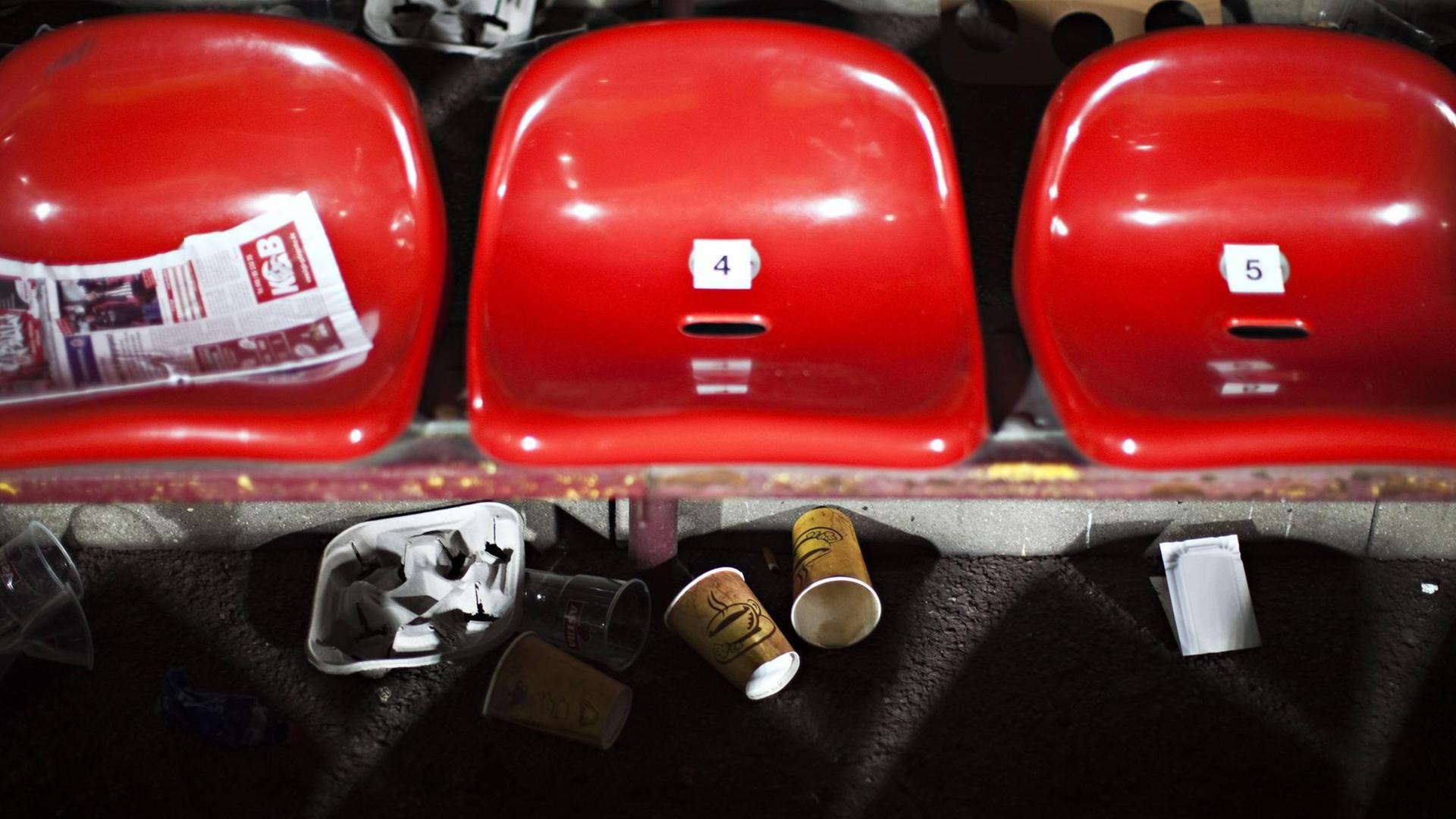 Rote Sitzschalen einer Stadiontribüne mit liegengelassenen Papp- und Plastikbechern. Rote Sitzschalen einer Stadiontribüne mit liegengelassenen Papp- und Plastikbechern.