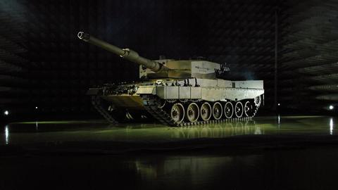 Fotografie eines frontal angeleuchteten Leopard 2A4 Panzers in einer dunklen Halle.