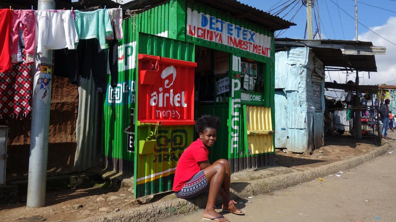 Eine M-Pesa-Agentur im Slum Mathare in Nairobi. Eine Frau sitzt vor Wellblech-Kiosk. Eine M-Pesa-Agentur im Slum Mathare in Nairobi. Eine Frau sitzt vor Wellblech-Kiosk.