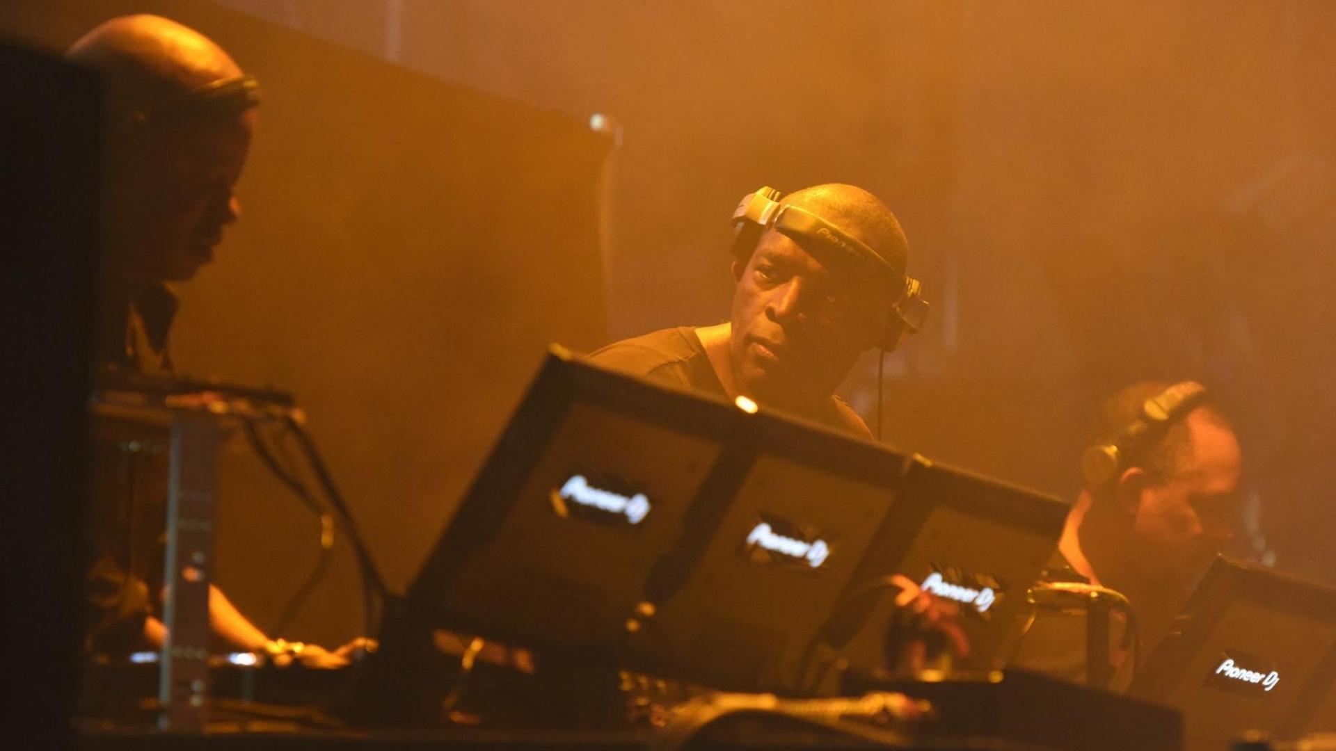 Drei DJs stehen an ihren Plattenspielern in einem abgedunkelten Raum und legen auf. Drei DJs stehen an ihren Plattenspielern in einem abgedunkelten Raum und legen auf.