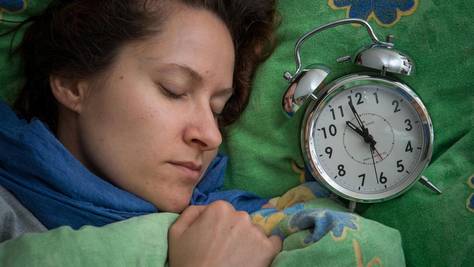 Eine Frau schläft im Bett, neben ihr liegt ein Wecker. Eine Frau schläft im Bett, neben ihr liegt ein Wecker.