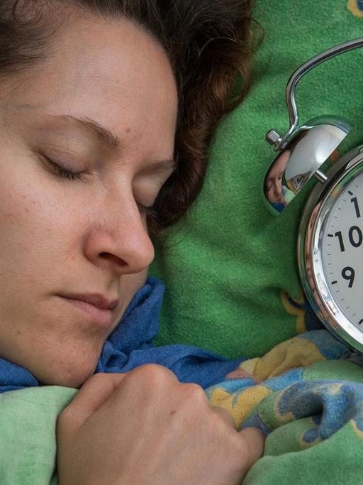 Eine Frau schläft im Bett, neben ihr liegt ein Wecker.