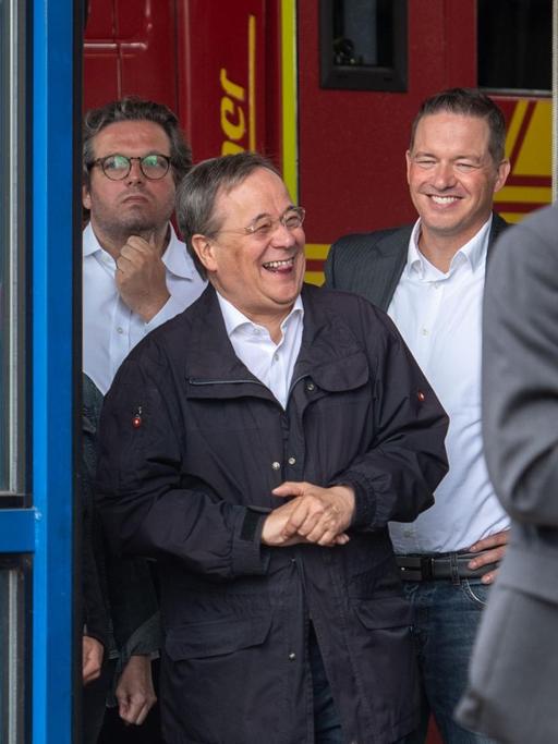Armin Laschet (2. v.l., CDU), Ministerpräsident von Nordrhein-Westfalen, lacht während Bundespräsident Steinmeier (nicht im Bild) im Hochwassergebiet in Erftstadt ein Pressestatement gibt.