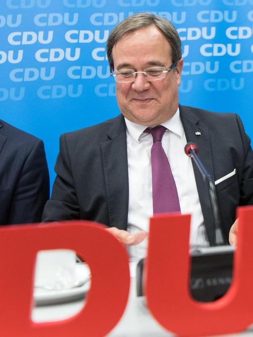 Jens Spahn, Armin Laschet und Friedrich Merz sitzen an einem Tisch, im Vordergrund sieht man groß die roten Buchstaben "CDU"
