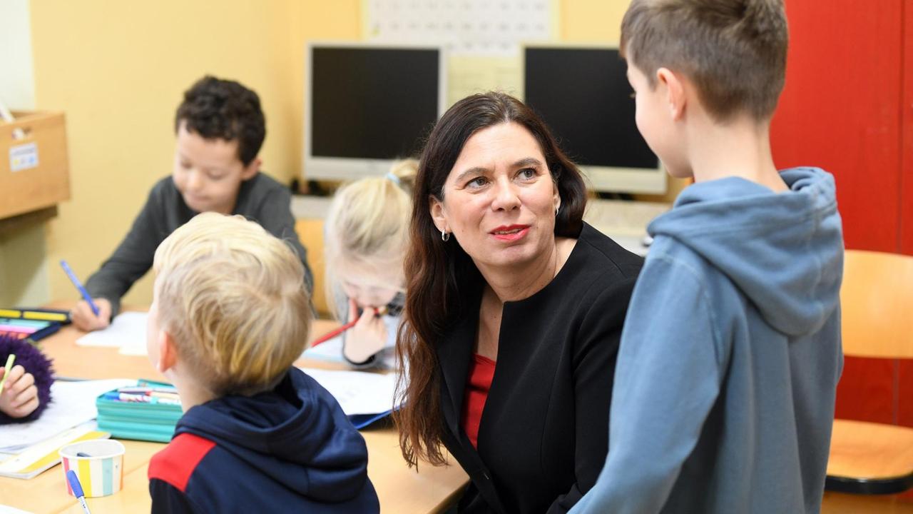 Sandra Scheeres sitzt an einem Gruppentisch in einer Schule und spricht mit einem Kind. Sandra Scheeres sitzt an einem Gruppentisch in einer Schule und spricht mit einem Kind.