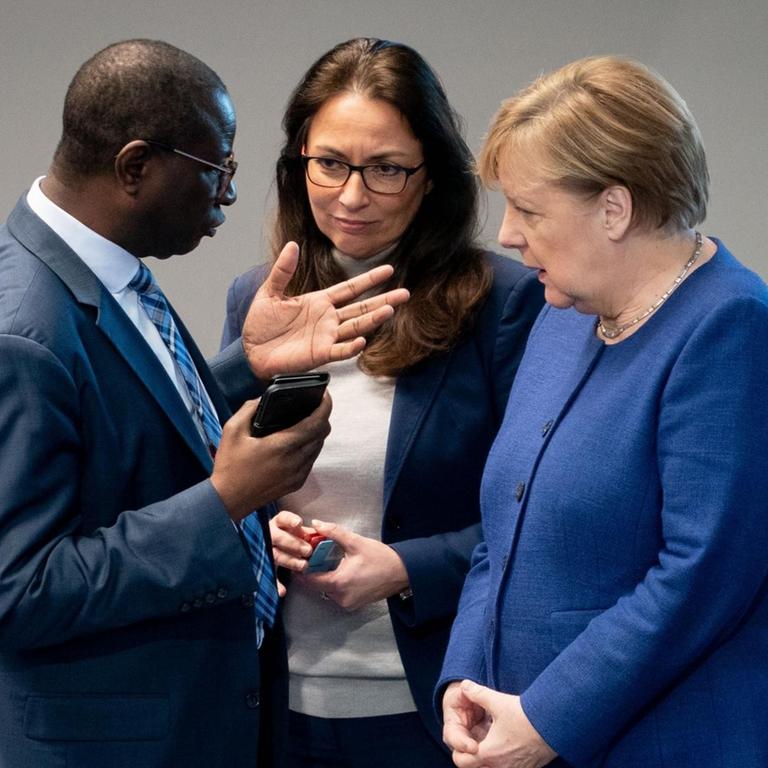 Die Bundeskanzlerin Angela Merkel unterhält sich bei der Sitzung des Bundestages mit den SPD-Bundestagsabgeordneten Karamba Diaby und Yasmin Fahimi.