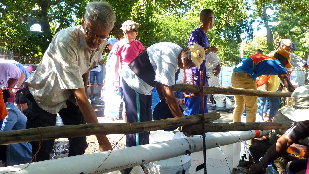 entlang eines Wasserrohrs stehen Menschen in der Schlange mit Kanistern entlang eines Wasserrohrs stehen Menschen in der Schlange mit Kanistern