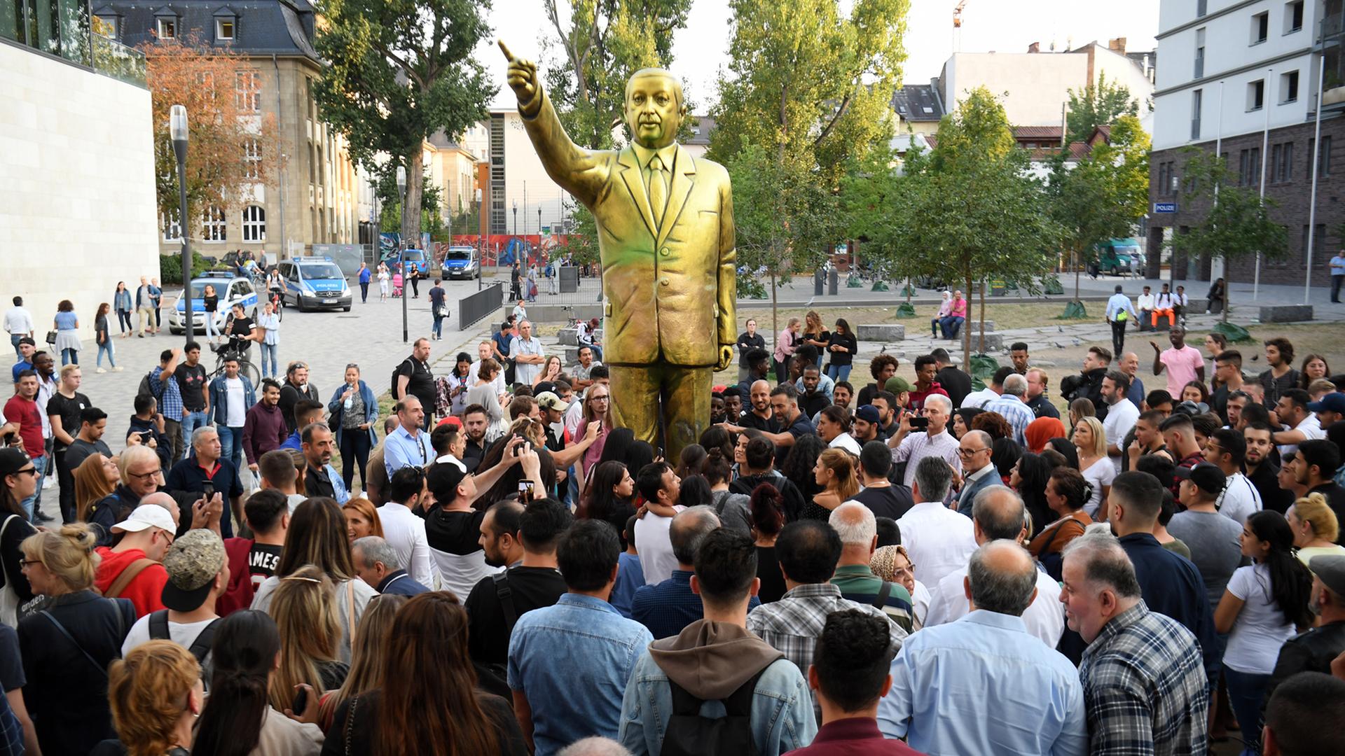 Zahlreiche Menschen haben sich auf dem Platz der Deutschen Einheit vor einer goldenen Erdogan-Statue in Wiesbaden versammelt. Die Statue wurde im Rahmen des Kunstfestivals "Wiesbaden Biennale" aufgestellt.