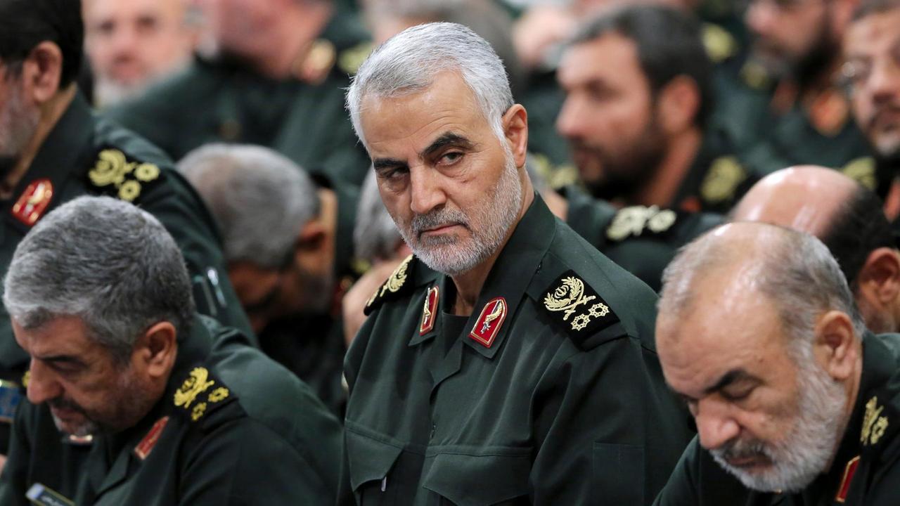 Soleimani mit ernstem Blick und in grüner Uniform zwischen weiteren Generälen. Er blickt zur Seite. 