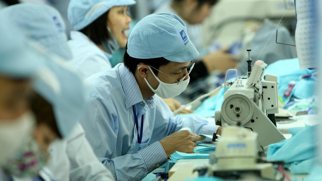 In einer Fabrikahalle sitzt ein vietnamesischer Näher an einer Nähmaschine