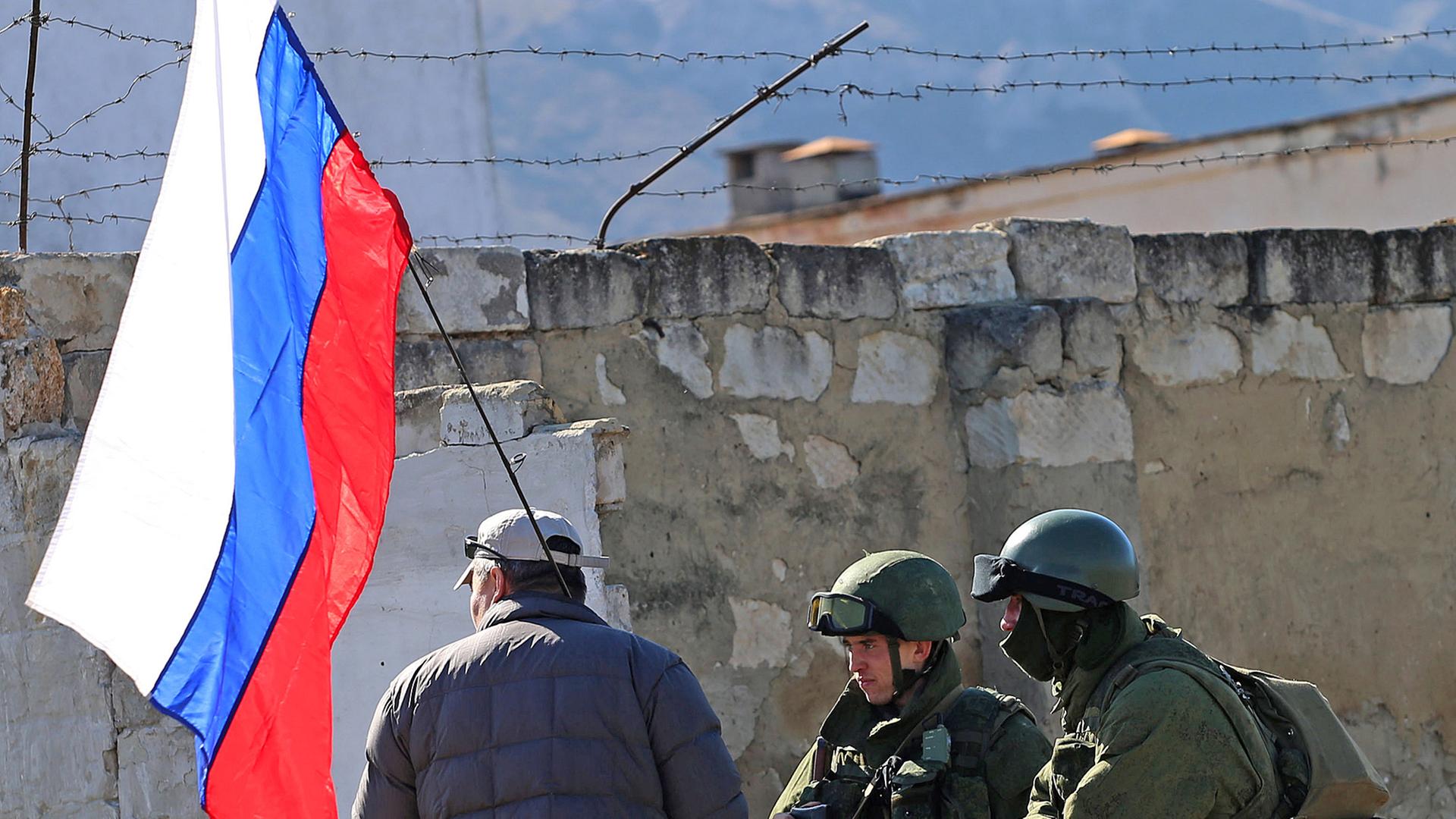 Mann mit russischer Fahne und zwei Soldaten auf der Krim (Aufnahme vom 3. März 2014)