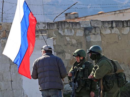Mann mit russischer Fahne und zwei Soldaten auf der Krim (Aufnahme vom 3. März 2014)