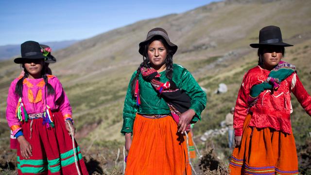 Drei Mädchen in traditionellen Gewändern und Hüten posieren während der Kartoffelernte für Fotos