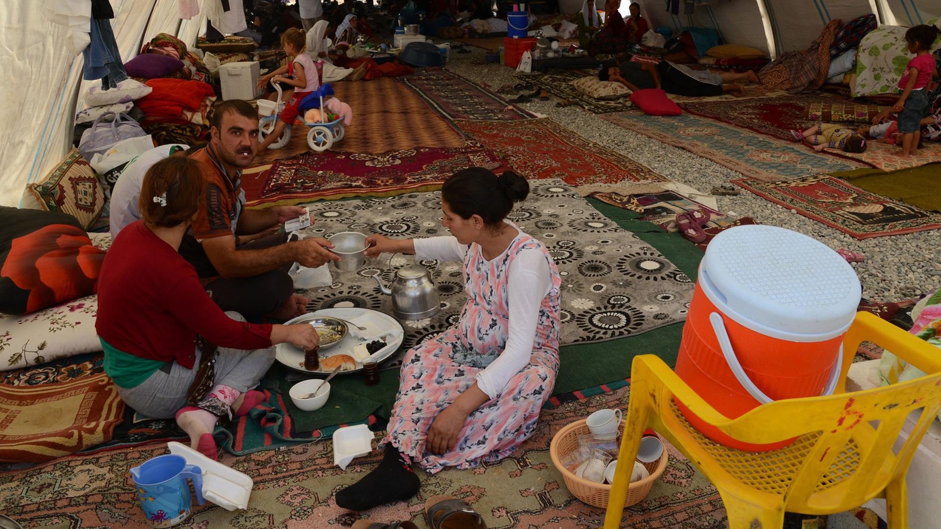 Eine jesidische Familie hat Schutz gefunden in einem Flüchtlingscamp in der Nähe der türkisch-irakischen Grenze. Erwachsene und Kinder sitzen auf ausgebreiteten Teppichen in einem Zelttunnel. Eine jesidische Familie hat Schutz gefunden in einem Flüchtlingscamp in der Nähe der türkisch-irakischen Grenze. Erwachsene und Kinder sitzen auf ausgebreiteten Teppichen in einem Zelttunnel.