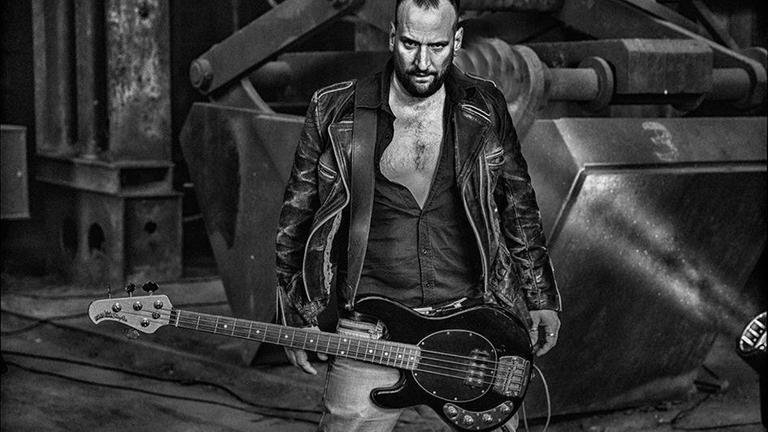 Der Sänger steht mit Gitarre und in Lederjacke auf einer großen Bühne. Der Sänger steht mit Gitarre und in Lederjacke auf einer großen Bühne.