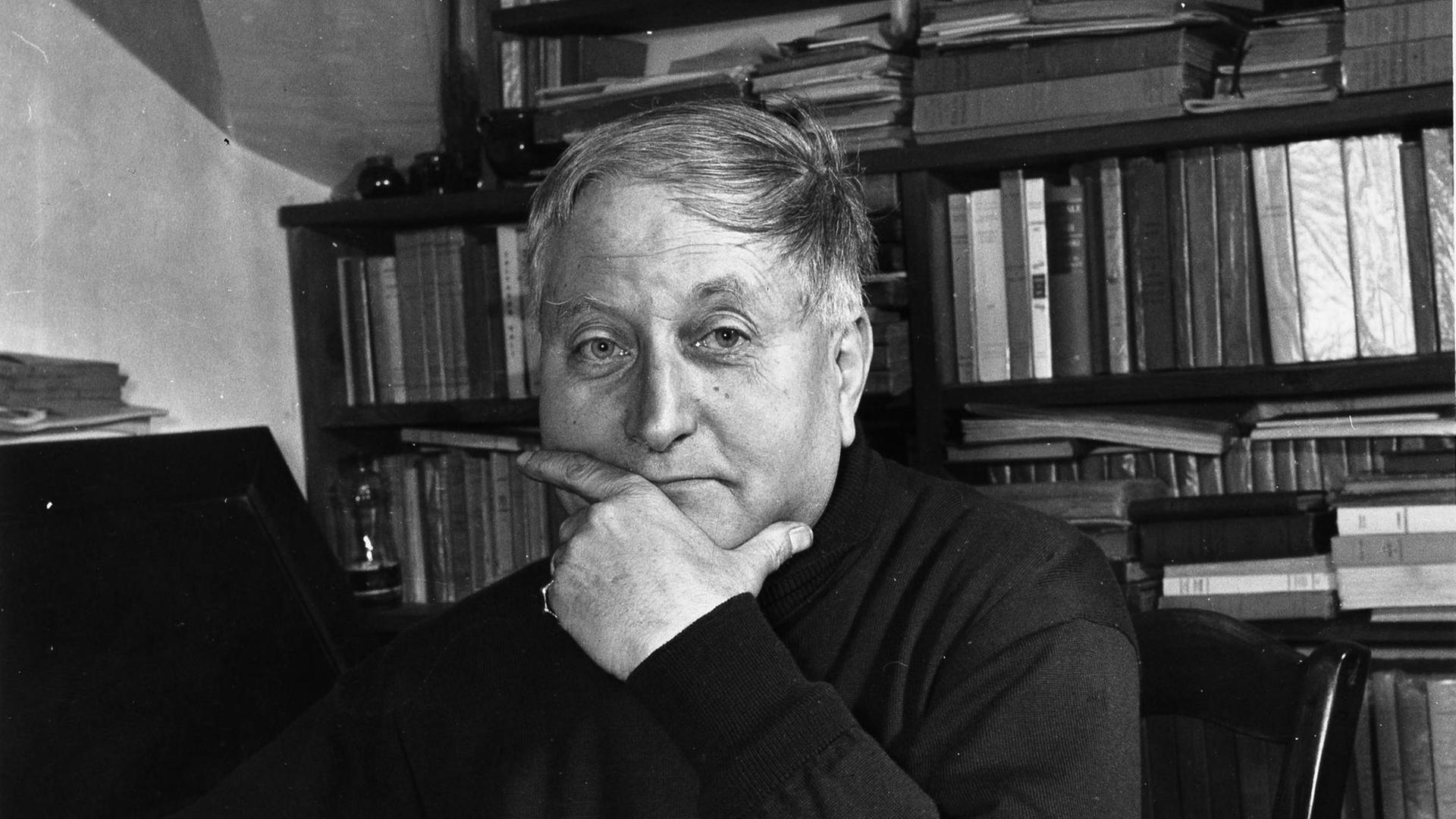 in schwarz-weiß Porträt-Foto des Schriftstellers Jean Giono an seinem Schreibtisch mit Pfeife und vor vollem Bücherregal. dans sa maison de Manosque. ©Renaud/Leemage |