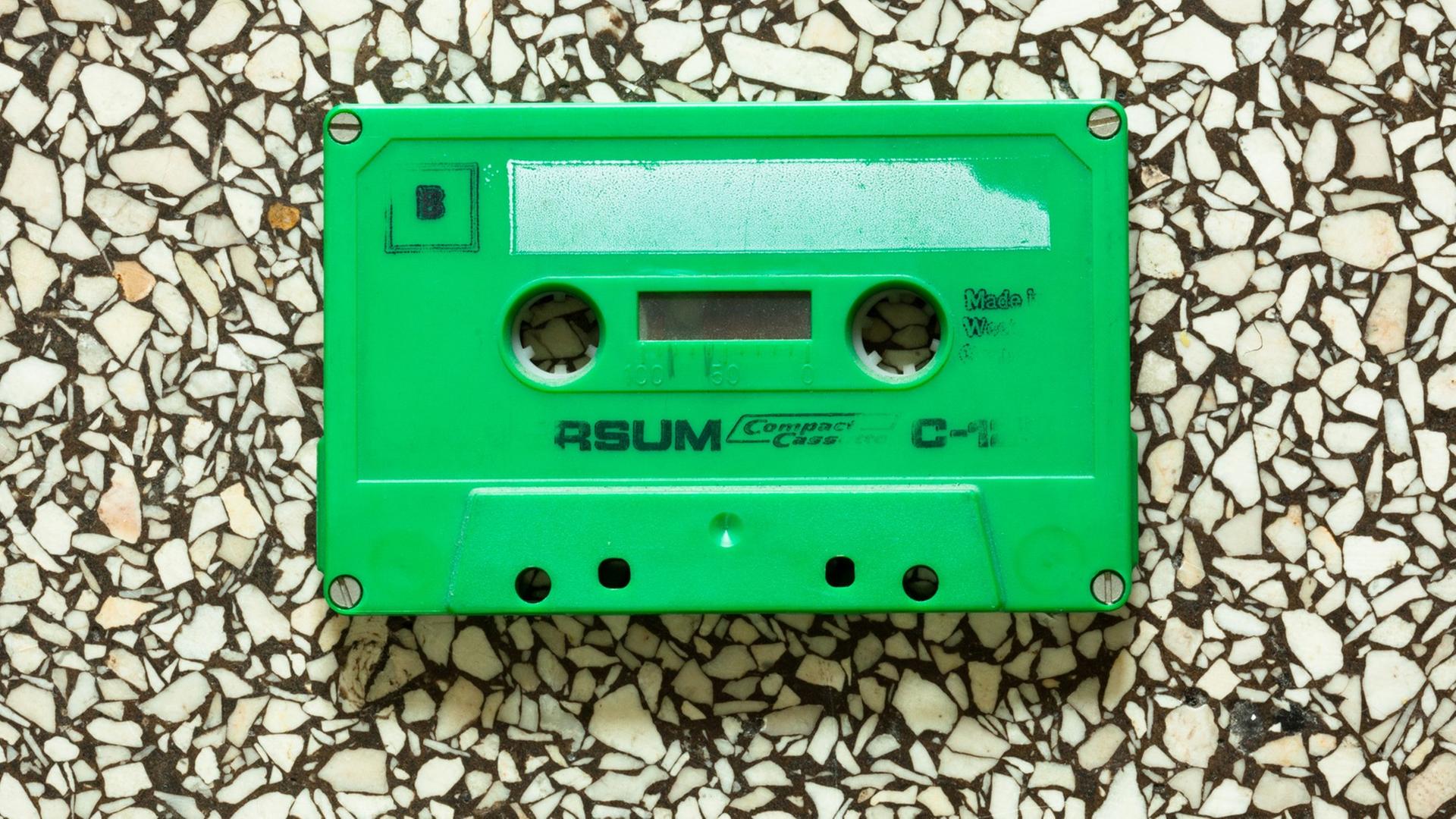 Eine grüne Kassette aus den 1970er-Jahren liegt auf einem Terrazzo-Steinboden. Eine grüne Kassette aus den 1970er-Jahren liegt auf einem Terrazzo-Steinboden.