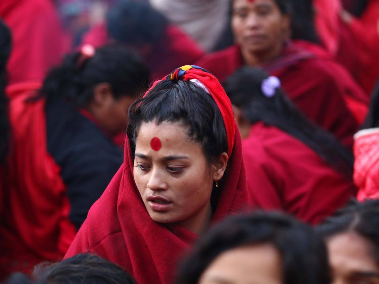 Viele nepalesische Hindu Frauen in roten Umhängen versammeln sich bei einem Gottesdient nahe dem heiligen Shalinadi Fluss am ersten Tag des Madhav Narayan Festes in Kathamandu, Nepal im Januar 2015. Die Frau im Zentrum betet zu ihren Gott Swasthani für den Wohlstand ihrer Familie und wünscht sich ein langes Leben für ihren Ehemann.