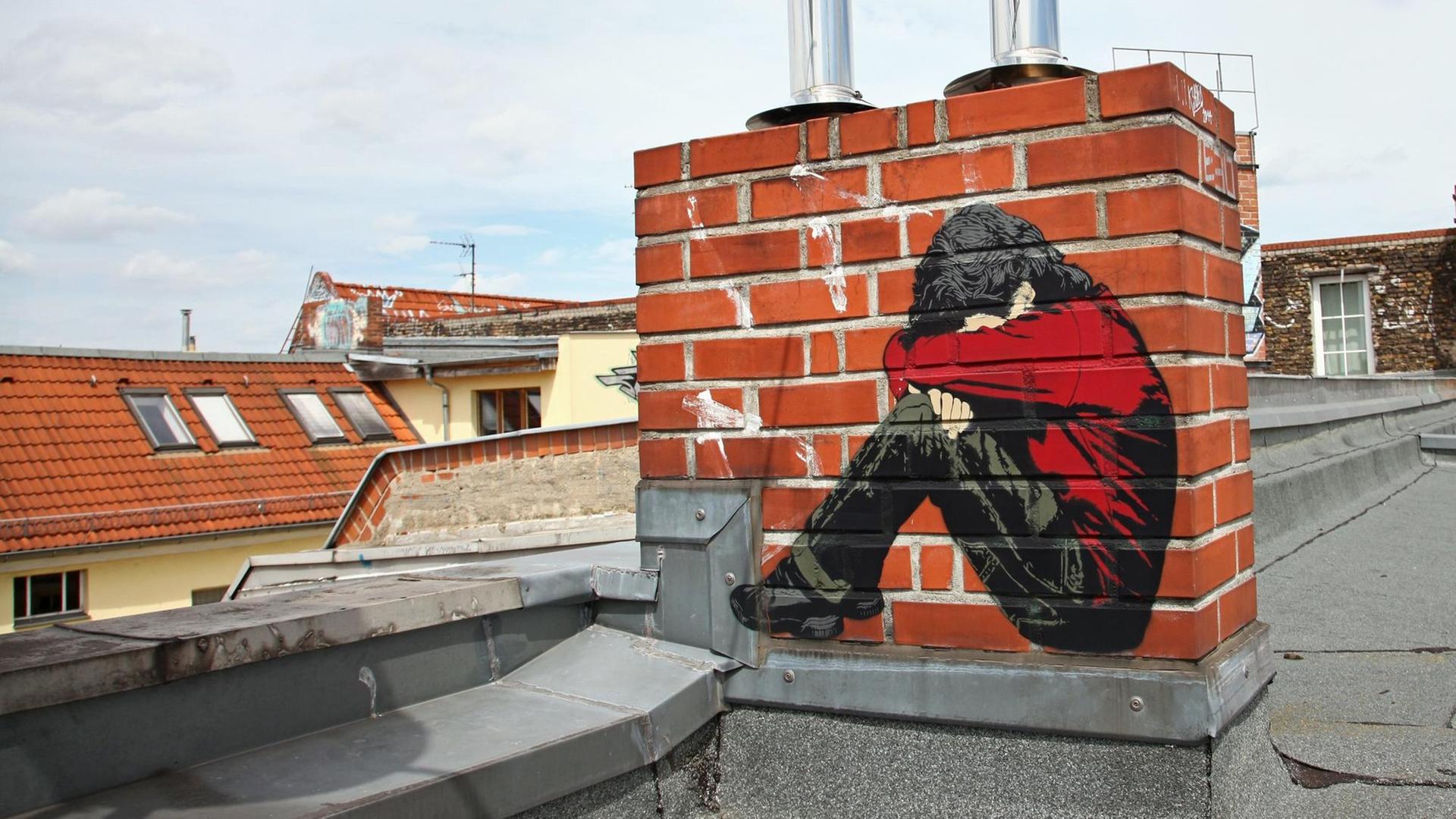 Ein Bild des Street-Art-Künstlers "Alias" auf einem Schornstein auf einem Dach - ein Junge, der sein Gesicht in seine Arme presst. Ein Bild des Street-Art-Künstlers "Alias" auf einem Schornstein auf einem Dach - ein Junge, der sein Gesicht in seine Arme presst.
