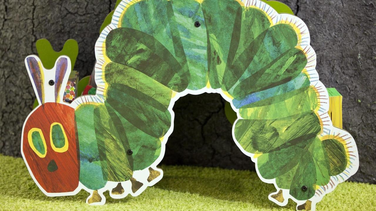 Die kleine grüne Raupe Nimmersatt aus Papier kriecht über einen Tisch in einer Buchhandlung. Die kleine grüne Raupe Nimmersatt aus Papier kriecht über einen Tisch in einer Buchhandlung.