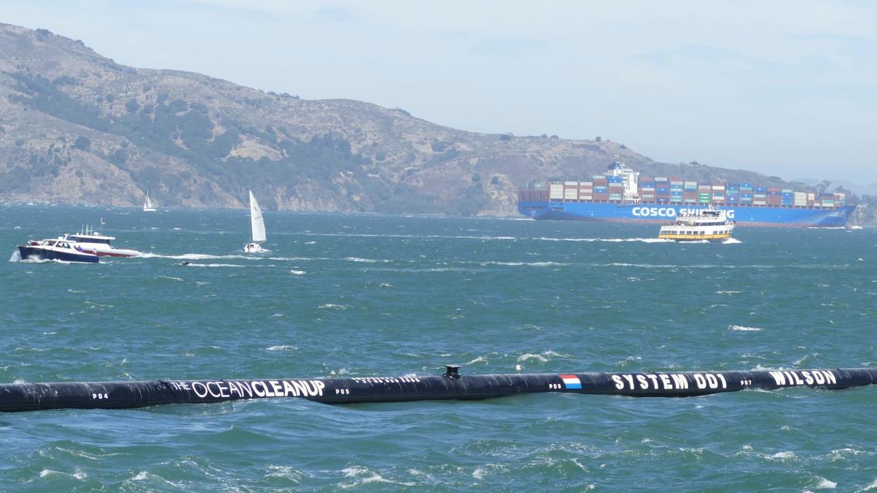 08.09.2018,USA, San Francisco: Das erste schwimmende Abfallsammelgerät "The Ocean Cleanup" ist auf seinem Weg zum Pazifischen Ozean in der Bucht von San Francisco zu sehen. Wie Fangarme sollen sich die Enden des 600 Meter langen Kunststoffrohrs des Reinigungssystems um Berge von Plastikmüll legen - zunächst auf dem Pazifik zwischen Kalifornien und Hawaii. Foto: Barbara Munker/dpa | Verwendung weltweit 08.09.2018,USA, San Francisco: Das erste schwimmende Abfallsammelgerät "The Ocean Cleanup" ist auf seinem Weg zum Pazifischen Ozean in der Bucht von San Francisco zu sehen. Wie Fangarme sollen sich die Enden des 600 Meter langen Kunststoffrohrs des Reinigungssystems um Berge von Plastikmüll legen - zunächst auf dem Pazifik zwischen Kalifornien und Hawaii. Foto: Barbara Munker/dpa | Verwendung weltweit