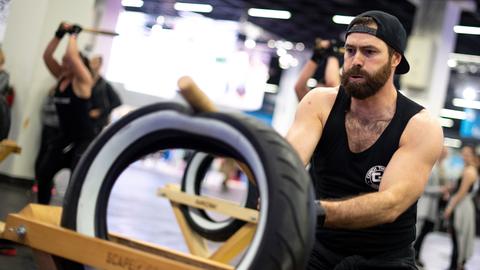 Ein Mann schlägt auf der weltgrößten Fitnessmesse Fibo bei einer Vorführung von "ScapeGoat" mit einem Schläger auf einen Reifen ein.