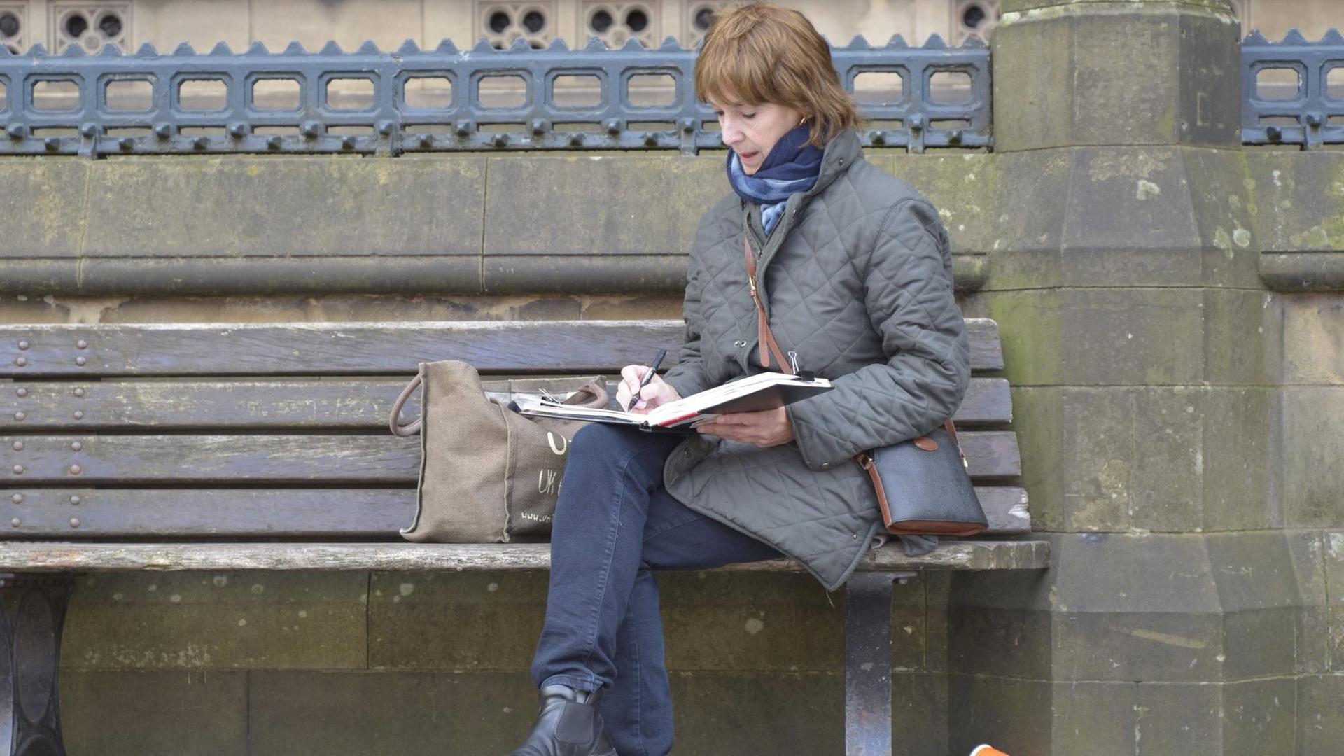 Eine Frau sitzt auf einer Parkbank und zeichnet