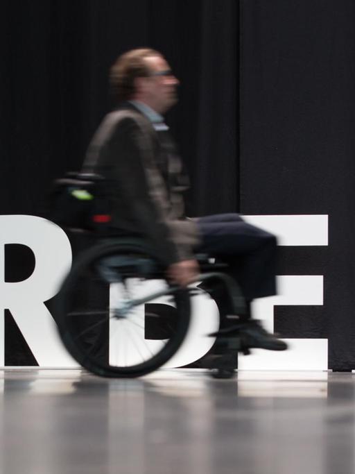 Ein Mensch mit Behinderung fährt am 20.02.2017 in Bielefeld mit seinem Rollstuhl an dem aufgestellten Wort "Arbeit" entlang.