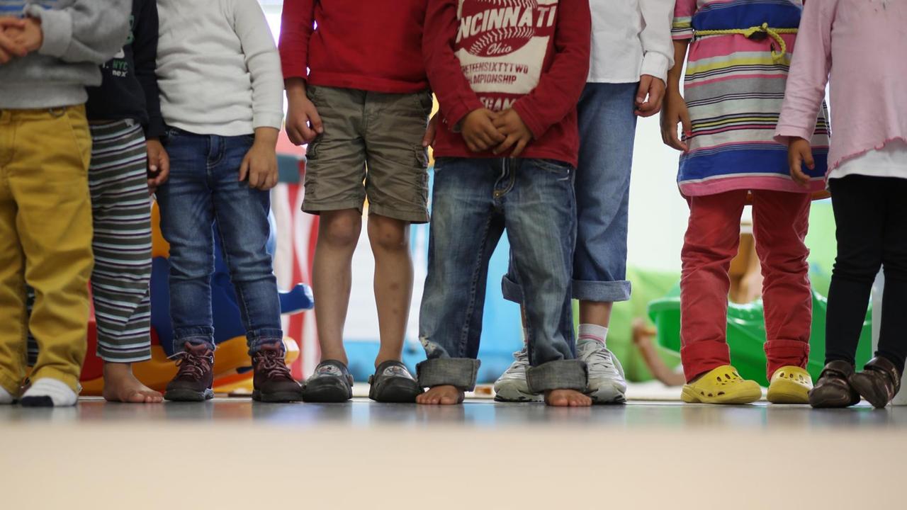 Acht Kinder stehen nebeneinander in der Kita, man sieht nur die Oberkörper und verdreckten Beine Acht Kinder stehen nebeneinander in der Kita, man sieht nur die Oberkörper und verdreckten Beine