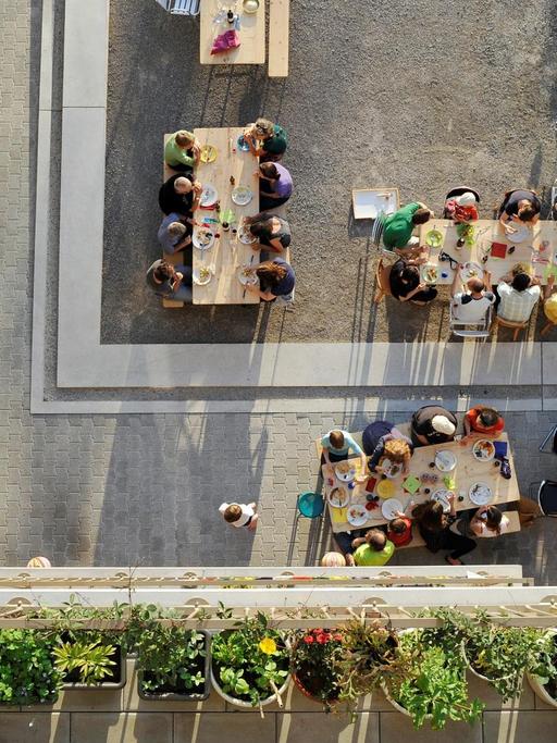 Draufsicht auf viele Menschen, die in einem offenen Innenhof in der Heizenholz Siedlung in Zürich gemeinsam an mehreren Tischen essen. Bild: Katrin Simonett