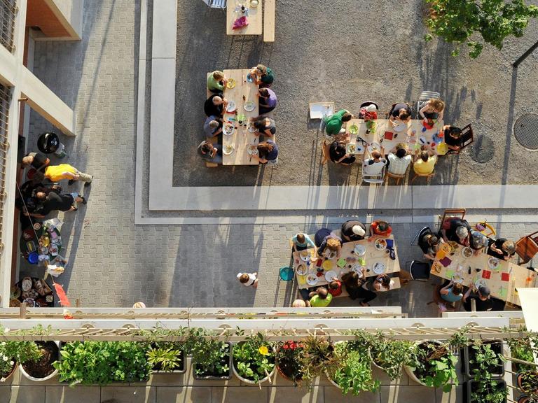 Draufsicht auf viele Menschen, die in einem offenen Innenhof in der Heizenholz Siedlung in Zürich gemeinsam an mehreren Tischen essen. Bild: Katrin Simonett