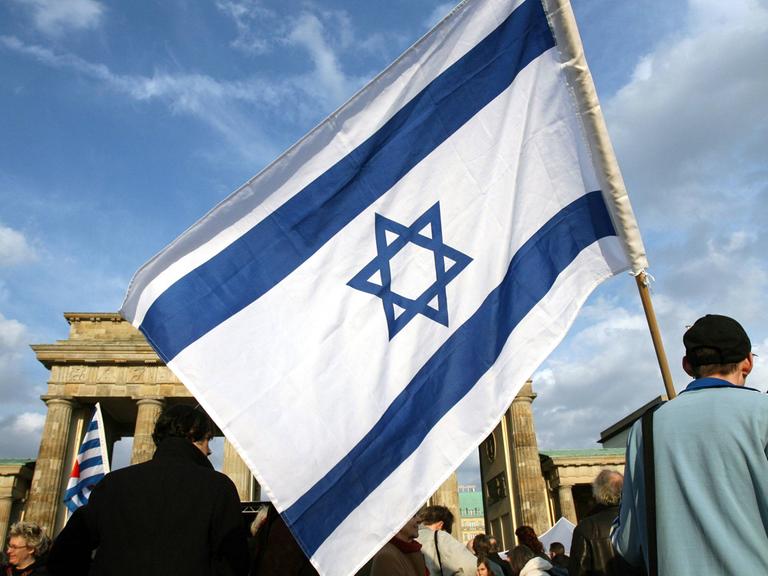 Ein Mann mit einer israelischen Fahne steht in Berlin am Brandenburger Tor.