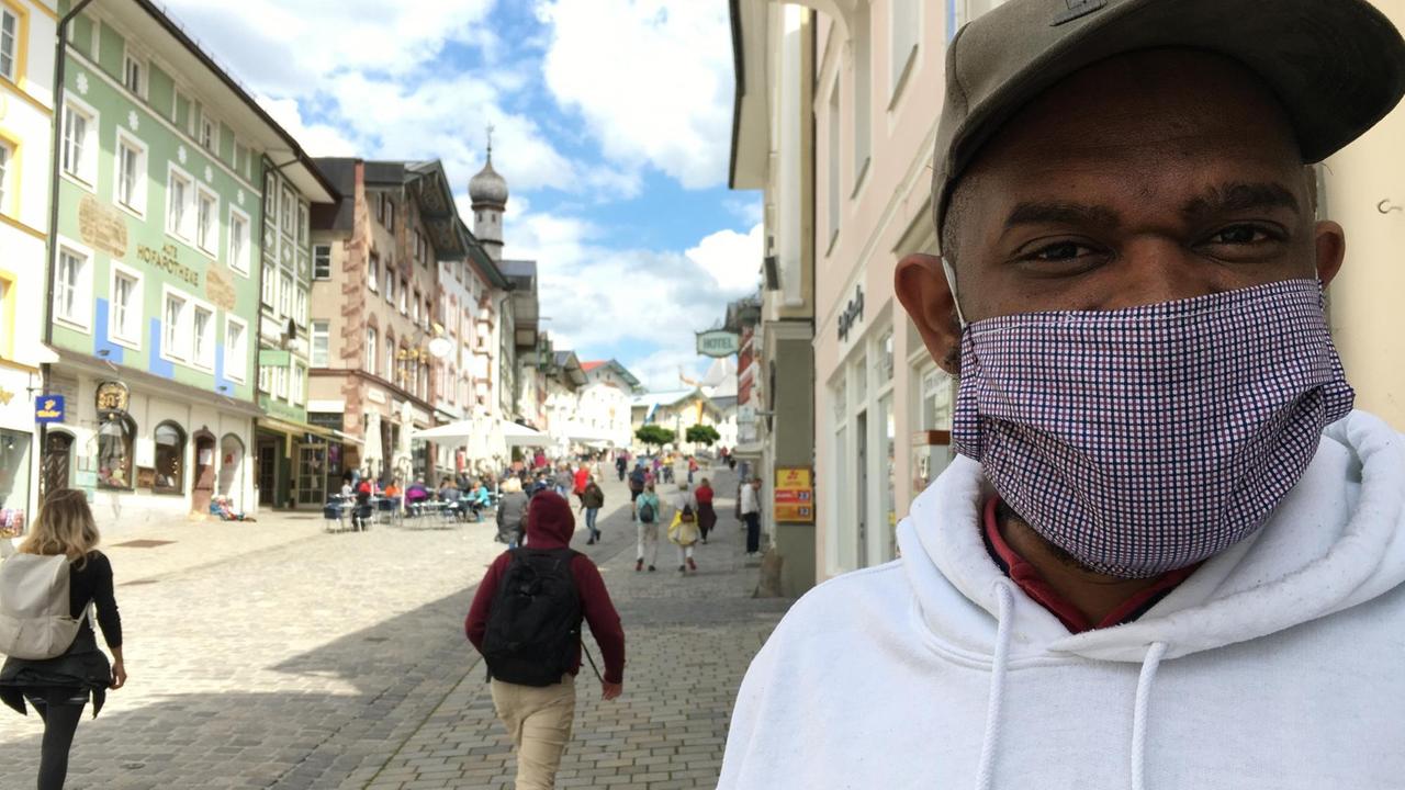 Fußgängerzone einer Kleinstadt, am Bildrand steht der senegalesische Geflüchtete mit einem Mundschutz. Fußgängerzone einer Kleinstadt, am Bildrand steht der senegalesische Geflüchtete mit einem Mundschutz.