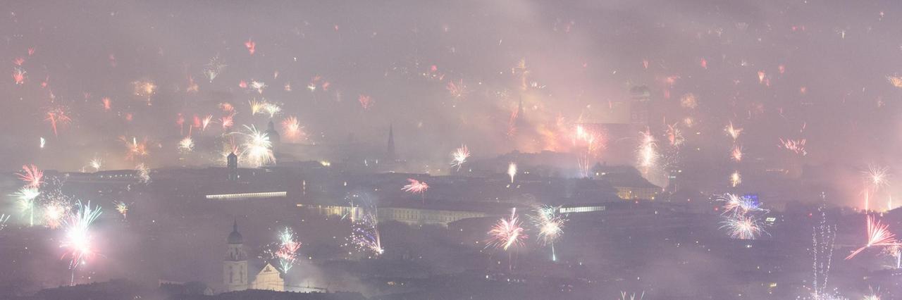 Feuerwerksraketen explodieren in der Silvesternacht über München und hüllen die Innenstadt in dichten Rauch.