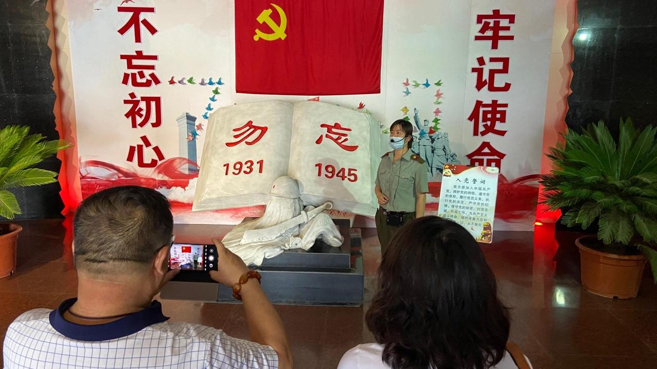 Zwei Museumsbesucher vor einem Marmorbuch und einer roten Flagge im chinesischen Weltkriegsmuseum in Hailar.