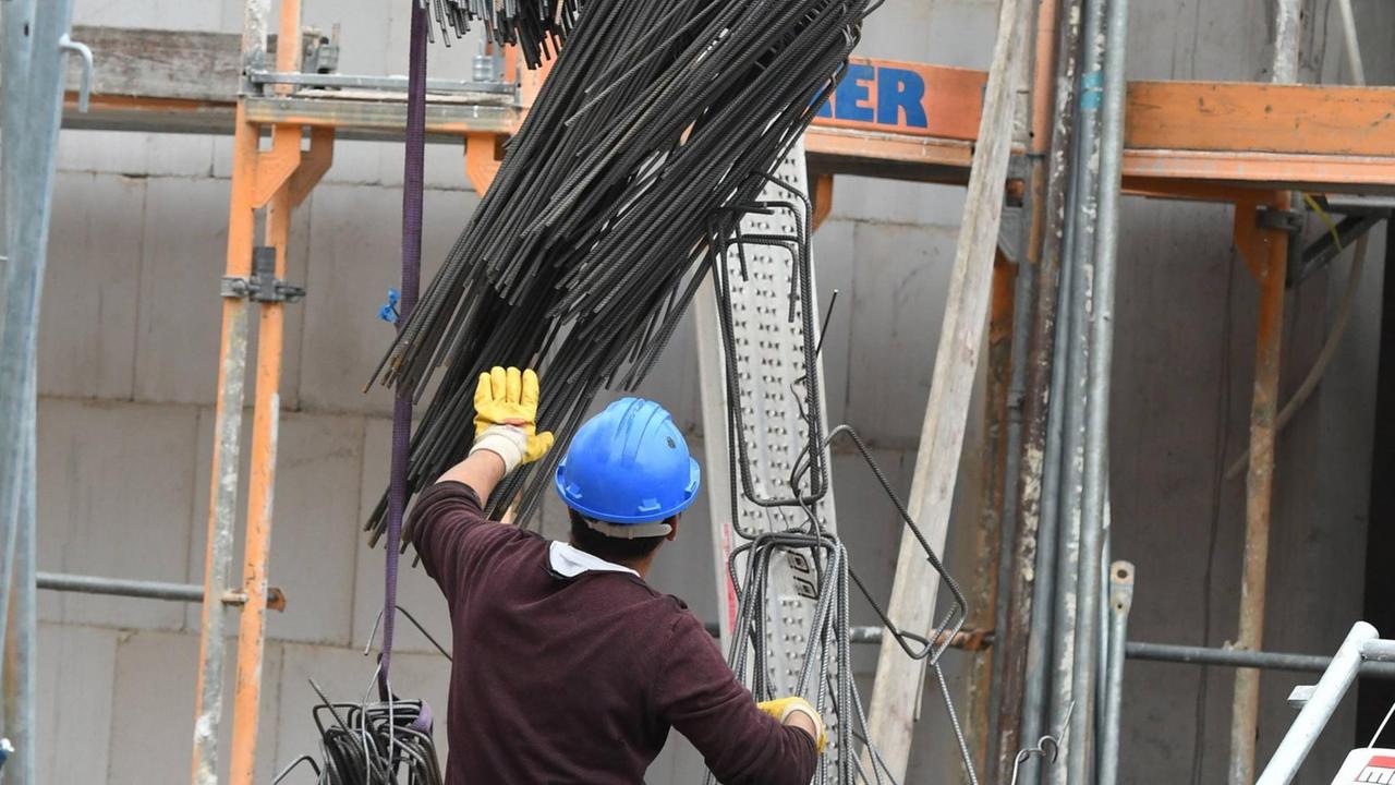 Ein Bauarbeiter bei der Arbeit auf der Baustelle. Er trägt einen Helm und steht mit dem Rücken zur Kamera. Ein Bauarbeiter bei der Arbeit auf der Baustelle. Er trägt einen Helm und steht mit dem Rücken zur Kamera.