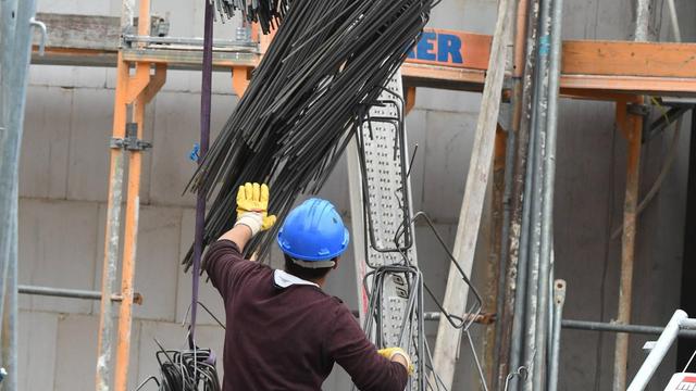 Ein Bauarbeiter bei der Arbeit auf der Baustelle. Er trägt einen Helm und steht mit dem Rücken zur Kamera. 