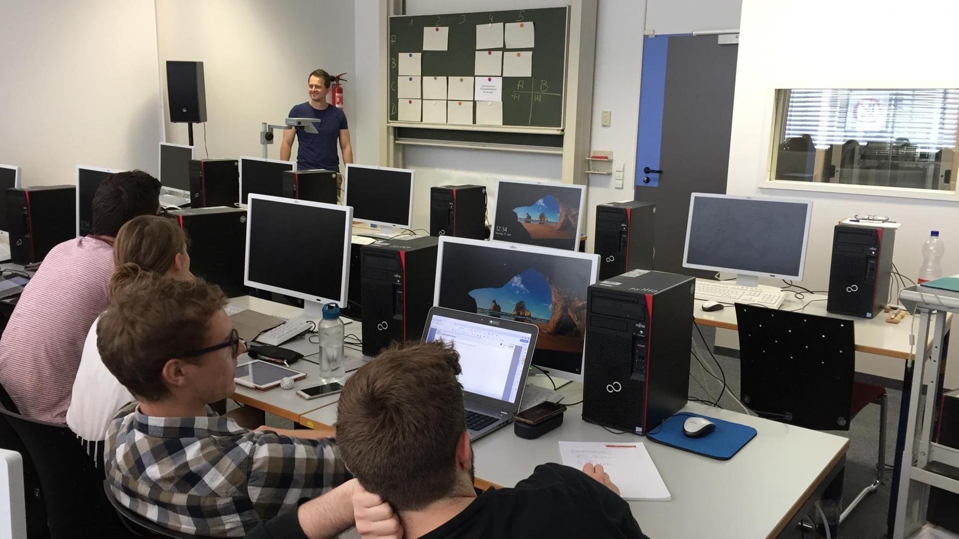 Der Dozent Dr. Stefan Fedtke steht im Computerraum und bespricht mit Studierenden ein Simulationsprojekt Der Dozent Dr. Stefan Fedtke steht im Computerraum und bespricht mit Studierenden ein Simulationsprojekt