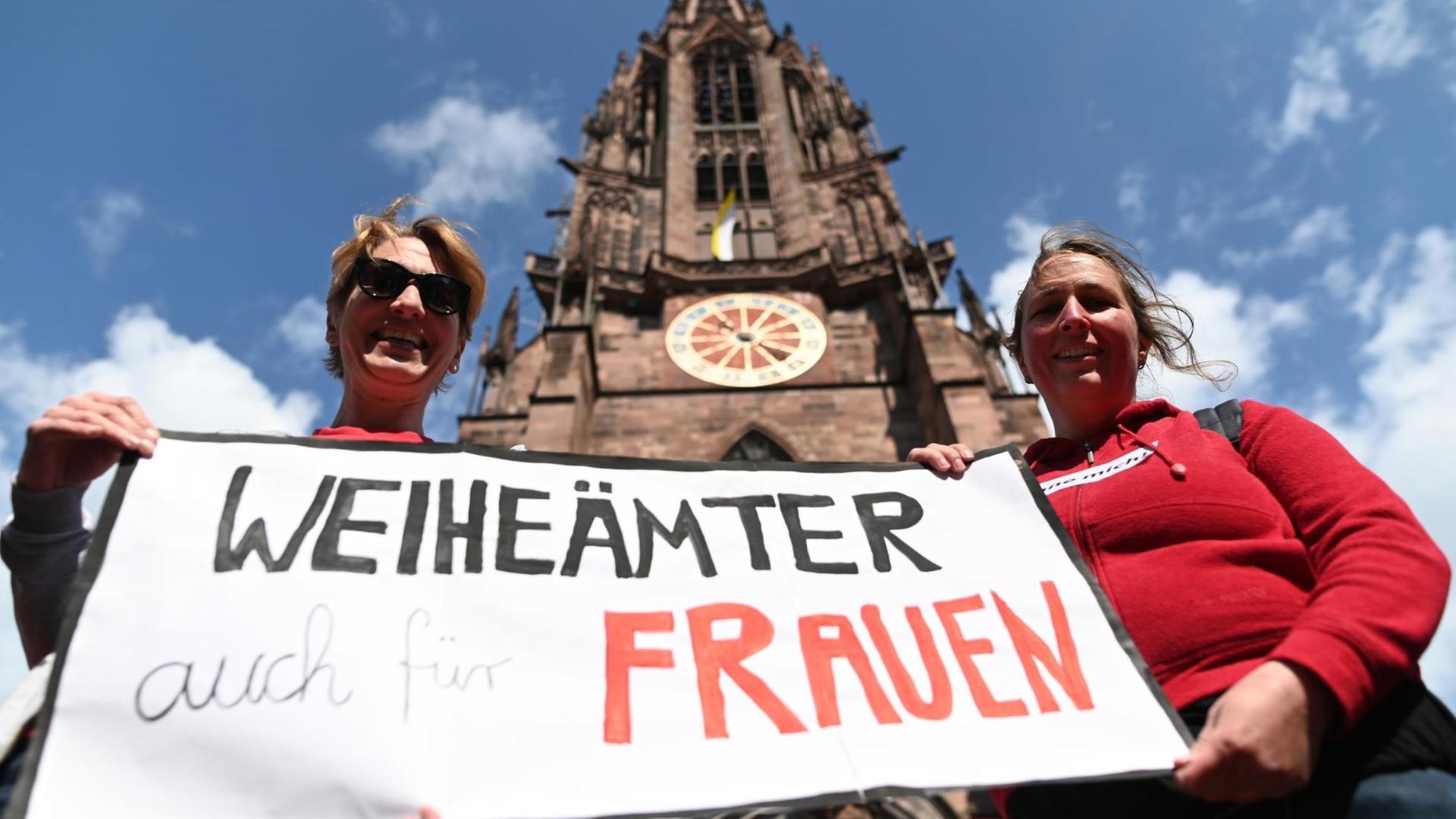 Zwei Frauen der Initiative Maria 2.0 der Katholische Frauengemeinschaft in der Erzdiözese Freiburg halten vor dem Freiburger Münster ein Banner mit der Aufschrift "Weiheämter auch für Frauen" in die Höhe. Zwei Frauen der Initiative Maria 2.0 der Katholische Frauengemeinschaft in der Erzdiözese Freiburg halten vor dem Freiburger Münster ein Banner mit der Aufschrift "Weiheämter auch für Frauen" in die Höhe.
