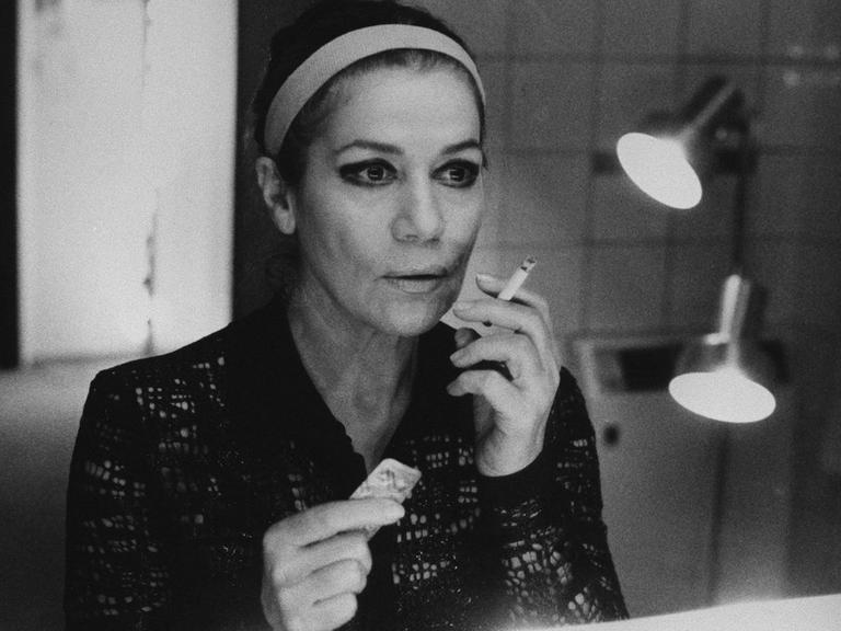 Hannelore Elsner hält in einer Hand eine Zigarette, in der anderen einen Streifen Tabletten. Sie schaut in den Spiegel.