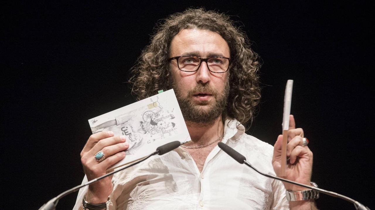 Ghayath Almadhoun steht bei einer Lesung an einem Rednerpult. Ghayath Almadhoun steht bei einer Lesung an einem Rednerpult.