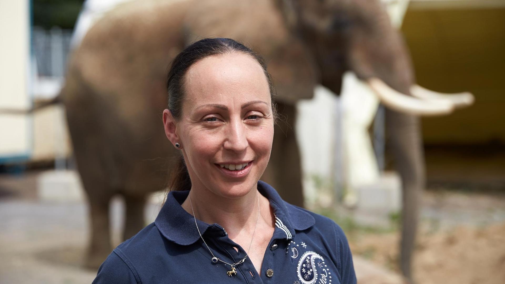 Zirkusdirektorin Jana Lacey-Krone lächelt für ein Foto, im Hintergrund die Elefantendame Kenia.