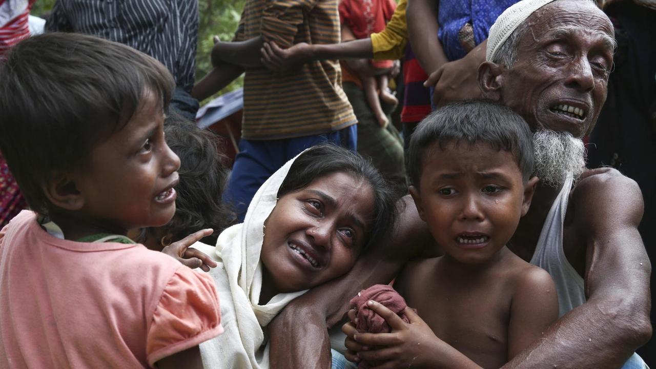 Das Bild zeigt eine Frau mit zwei Kindern und einen alten Mann, die sich weinend in den Armen halten. Dahinter sieht man weitere Menschen.
