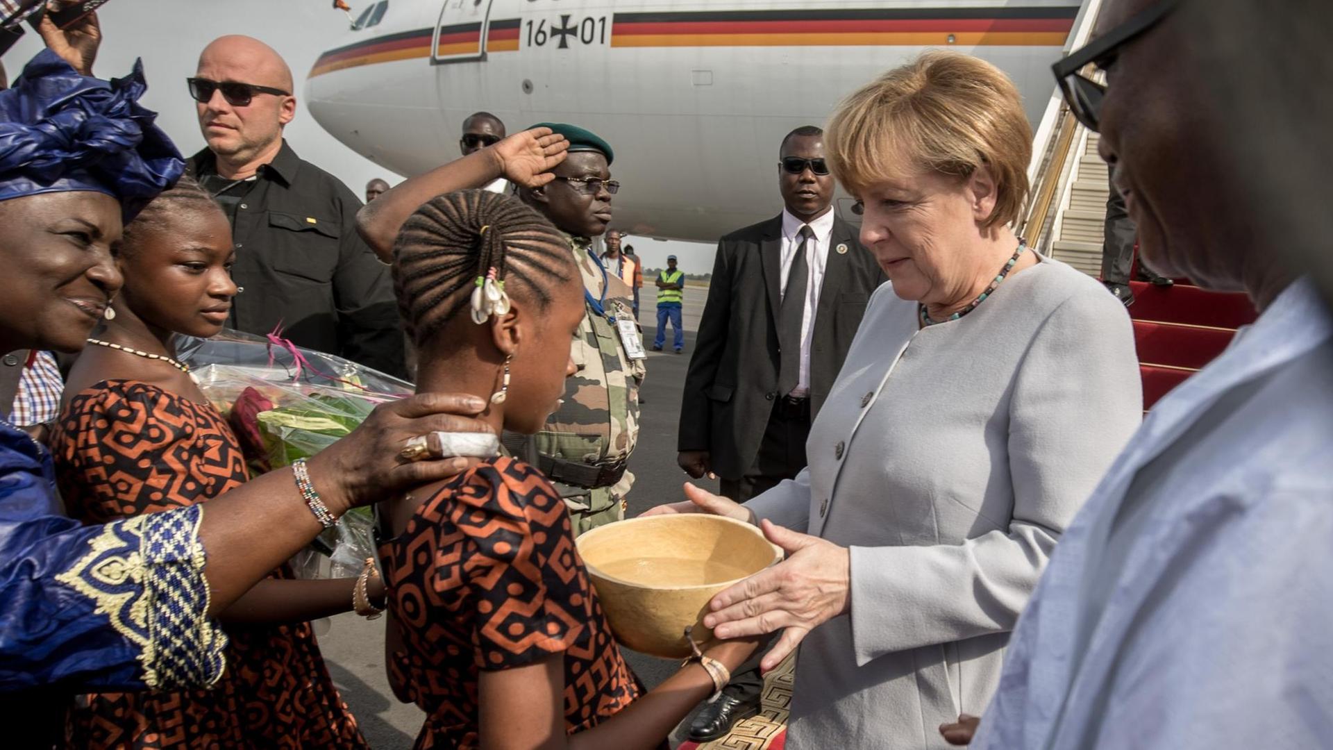 Bundeskanzlerin Angela Merkel (CDU) wird am 09.10.2016 in Bamako in Mali neben Staatspräsident Ibrahim Boubacar Keita (r) am Flughafen von Blumenmädchen begrüßt, die der Kanzlerin zunächst eine traditionelle Wasserkalebasse reichen. Bundeskanzlerin Angela Merkel (CDU) wird am 09.10.2016 in Bamako in Mali neben Staatspräsident Ibrahim Boubacar Keita (r) am Flughafen von Blumenmädchen begrüßt, die der Kanzlerin zunächst eine traditionelle Wasserkalebasse reichen.