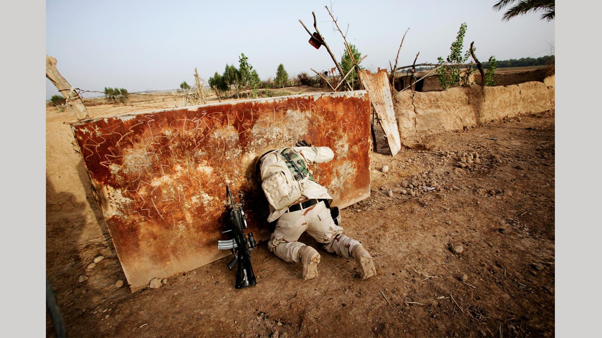 Ein US-Soldat sucht Waffen in einem ehemaligen Wassertank im Jahr 2005 im Irak - er ist von hinten zu sehen und steckt bis zu den Schultern in der Öffnung: Foto aus dem Bildband "hello camel" von Christoph Bangert über die Absurdität von Krieg Ein US-Soldat sucht Waffen in einem ehemaligen Wassertank im Jahr 2005 im Irak - er ist von hinten zu sehen und steckt bis zu den Schultern in der Öffnung: Foto aus dem Bildband "hello camel" von Christoph Bangert über die Absurdität von Krieg