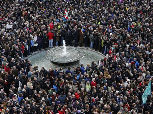 Dicht gedrängt stehen hunderte Menschen auf einem Platz, in ihrer Mitte ein Brunnen.