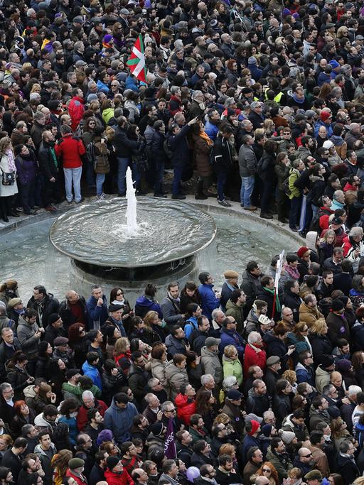 Dicht gedrängt stehen hunderte Menschen auf einem Platz, in ihrer Mitte ein Brunnen.