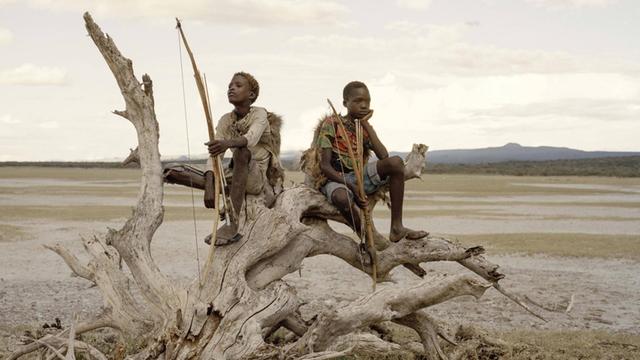 Am Eyasi-See in Tansania halten Osama (15) und Manu (14) Pfeil und Bogen in der Hand, während sie auf einem abgestorbenen Baum sitzen. Sie gehören den Hadza an, einer der letzten Gemeinschaften von Jägern und Sammlern.