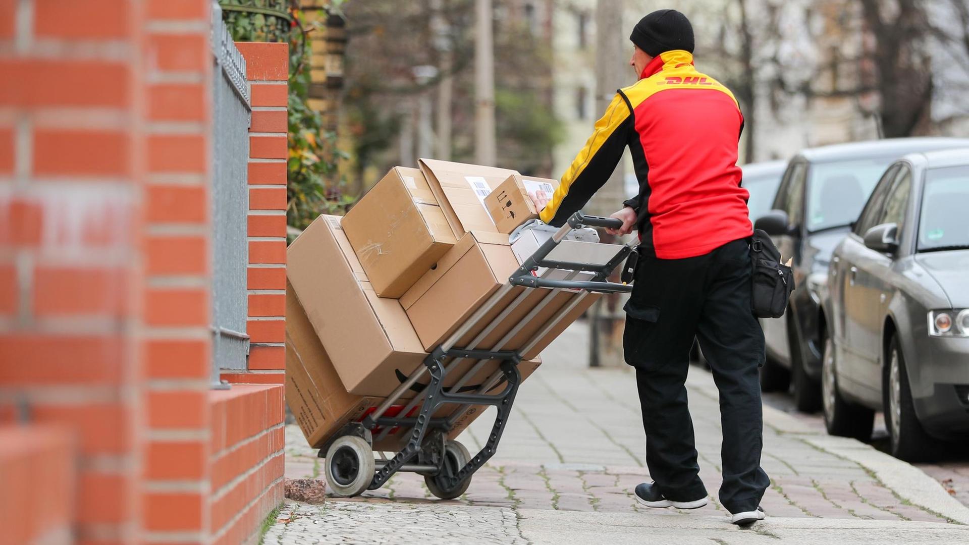 Ein DHL Paketzusteller geht mit einer Sackkarre voll Pakete zu einem Haus im Paulusviertel.