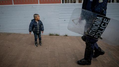 Ein kleiner Junge steht im Hafen der griechischen Insel Lesbos vor einem Polizisten